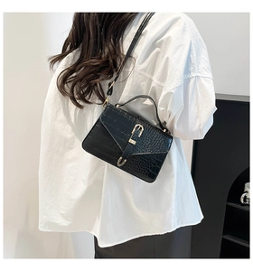 Détail d'un sac bandoulière noir motif crocodile avec boucle fer à cheval dorée sur mannequin