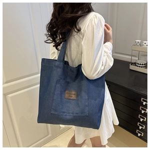 Detailed view of large dark blue denim tote bag with front pocket and leather label
