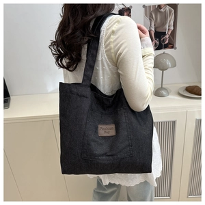Side view of large black canvas tote bag with brown leather patch shown on shoulder
