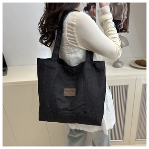 Close-up of black canvas tote bag with brown leather fashion label and woven texture