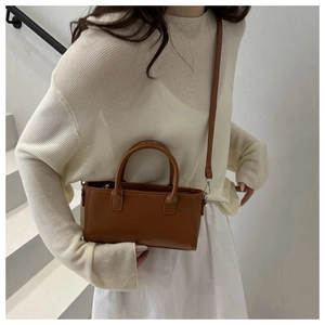 Brown vintage rectangular handbag shown on model against a minimalist white staircase