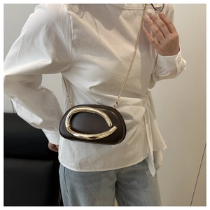 Detail of a dark brown leather clutch with a large gold wave buckle and a fine chain strap