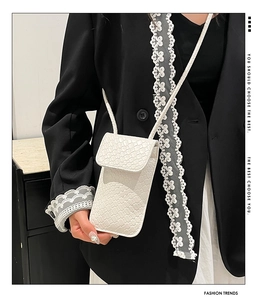Close-up of white woven leather phone bag worn on a black blazer for a modern fashion look