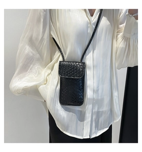 Close-up of black woven leather mini crossbody bag styled on a white silk shirt