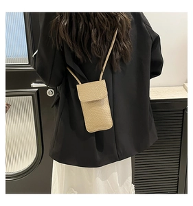 Close-up of a beige faux-crocodile texture phone crossbody bag worn by a model in a lifestyle setting