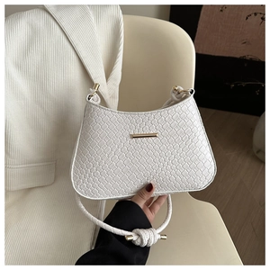 Detail of white crocodile texture baguette bag with woven knotted strap and gold hardware