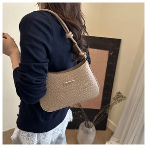 Detail of beige woven texture hobo bag featuring gold metal bar and knotted strap