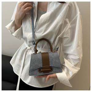 Side view of gray felt and brown leather crossbody bag worn by a model in a minimalist setting