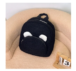 Close-up of black plush teddy bear backpack with cute ears on a soft beige sofa
