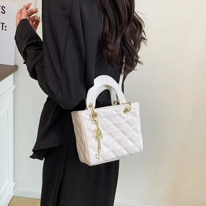 Borsa a mano trapuntata bianca con ciondolo dorato indossata come borsa a tracolla