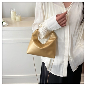 Detail of golden crescent handbag featuring elegant large pearl accents and metal chain strap