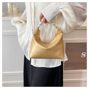 Detail of champagne gold satin bag featuring a luxury pearl handle and delicate metal chain