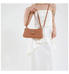 Détail d'un sac porté épaule marron tressé avec nœud en argent sur robe en soie