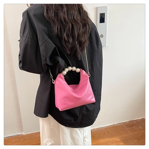 Detail of pink dumpling bag with pearl handle and golden chain worn by model