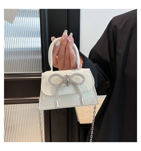 Close-up of a white glitter mini handbag with a sparkling rhinestone bow and silver chain strap