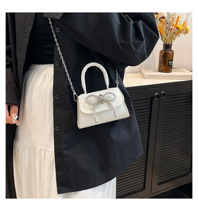 Close-up of white sequined mini bag with silver rhinestone bow and metal chain strap