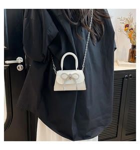 Détail du mini sac blanc avec un nœud en strass et une bandoulière chaîne