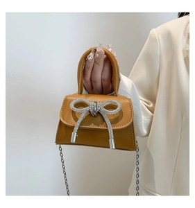 Close-up of brown faux leather mini bag featuring a sparkling rhinestone bow buckle and chain