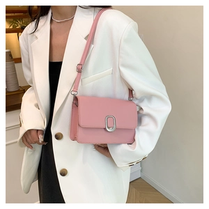 Detail shot of a pink leather crossbody bag with an oval silver buckle and adjustable strap