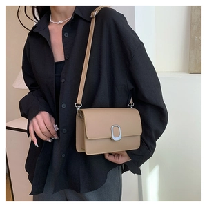 Detail of khaki PU leather crossbody square bag with a silver oval metal buckle on a model