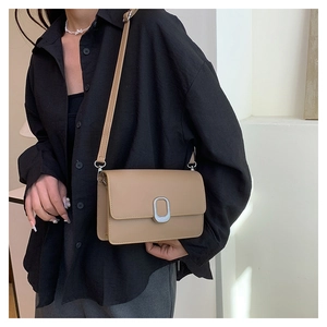Close-up of minimalist khaki square shoulder bag with oval metal buckle on model