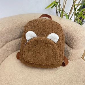 Cute brown plush teddy bear backpack with white ears on a textured sofa background