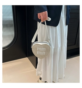 Detailed view of heart-shaped woven straw handbag with white letter embroidery and strap