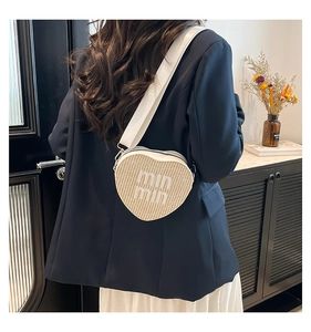 Detail of heart-shaped woven crossbody bag with min min text and wide white strap