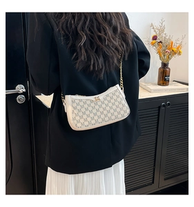 Chic beige underarm bag with M monogram print and gold chain strap shown on a model