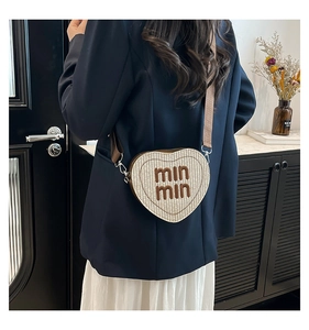 Detail of heart-shaped woven crossbody bag featuring min min lettering and brown strap