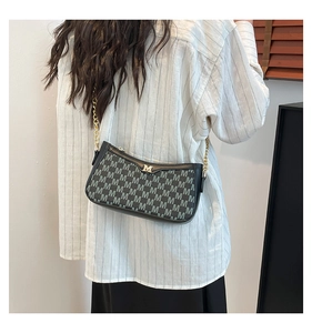 Detailed view of monogrammed crossbody bag with golden chain strap on model shoulder