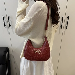 Red crescent shoulder bag with woven texture and gold bow detail on a model