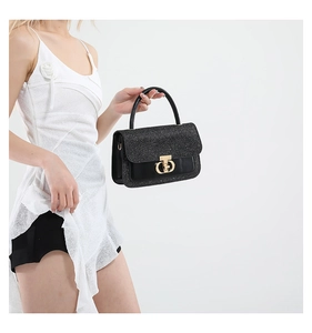 Detail of black sequin handbag with gold metal clasp and leather texture on a white dress