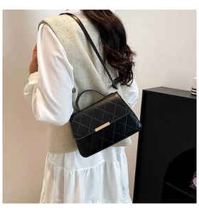 Close-up of black quilted shoulder bag with golden metal buckle and diamond stitching