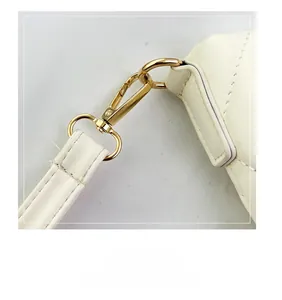 Dettaglio del gancio in metallo dorato e cuciture della tracolla in pelle sulla borsa crema