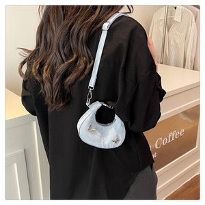 Modèle portant un sac selle bleu clair avec détails papillon en métal dans un café