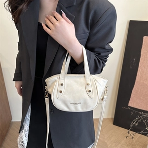 Elegant off-white mini bucket bag with gold hardware and logo, held by a model in a suit