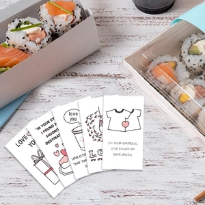 Fan-shaped display of romantic hand-drawn lunch box cards on a light wooden background