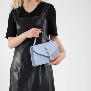 Petit sac à main bleu clair texturé avec boucle dorée porté par un mannequin