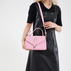 Petit sac carré rose avec boucle dorée et large bandoulière porté par un mannequin