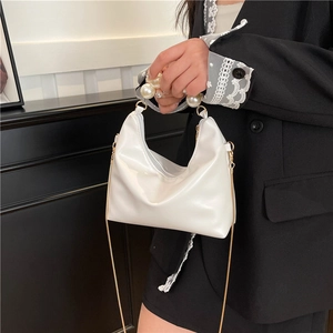 Mini white dumpling handbag with pearl handle and gold chain strap shown on black suit