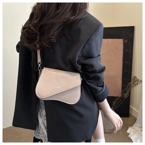 Detail view of beige saddle shoulder bag with silver logo and thin strap on a model