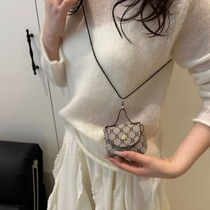 Detail of a mini monogrammed neck bag with vintage pattern and metal hook on white knitwear