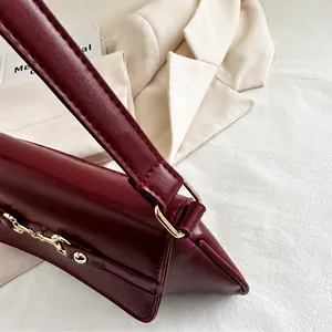 Detail der weinroten Lederschultertasche mit goldener Schnalle auf weißem Blazer