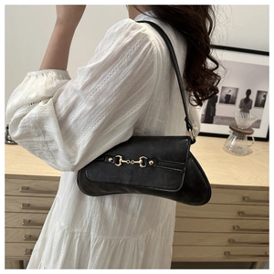 Schwarze matte Leder-Schultertasche mit goldener Trense vor wohnlichem Hintergrund