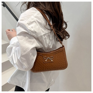 Brown woven texture underarm bag with a metal bow detail shown on a female model