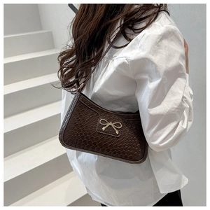 Detail of dark brown bow shoulder bag with crocodile pattern and metallic bow charm