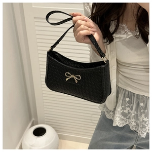 Detail of black woven underarm bag featuring a delicate gold bow metal accessory
