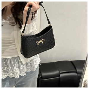 Close-up of black woven shoulder bag featuring a decorative gold bow and leather strap