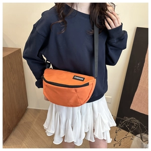 Orange nylon crossbody bag with black FASHION label shown on a model in a bright interior
